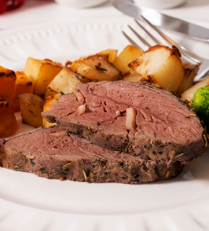 Medium-cooked lamb rump roast slices plated with roast potatoes